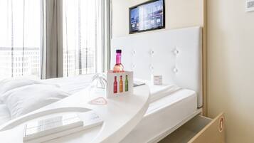 Habitación de hotel moderna con una cama curvada, una pantalla digital en la pared y vistas de la ciudad.