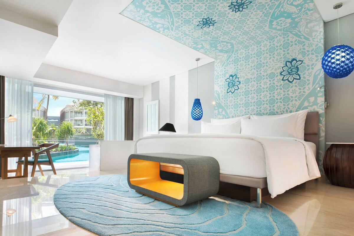 A modern hotel room with a large bed, a view of the pool, and a balcony.
