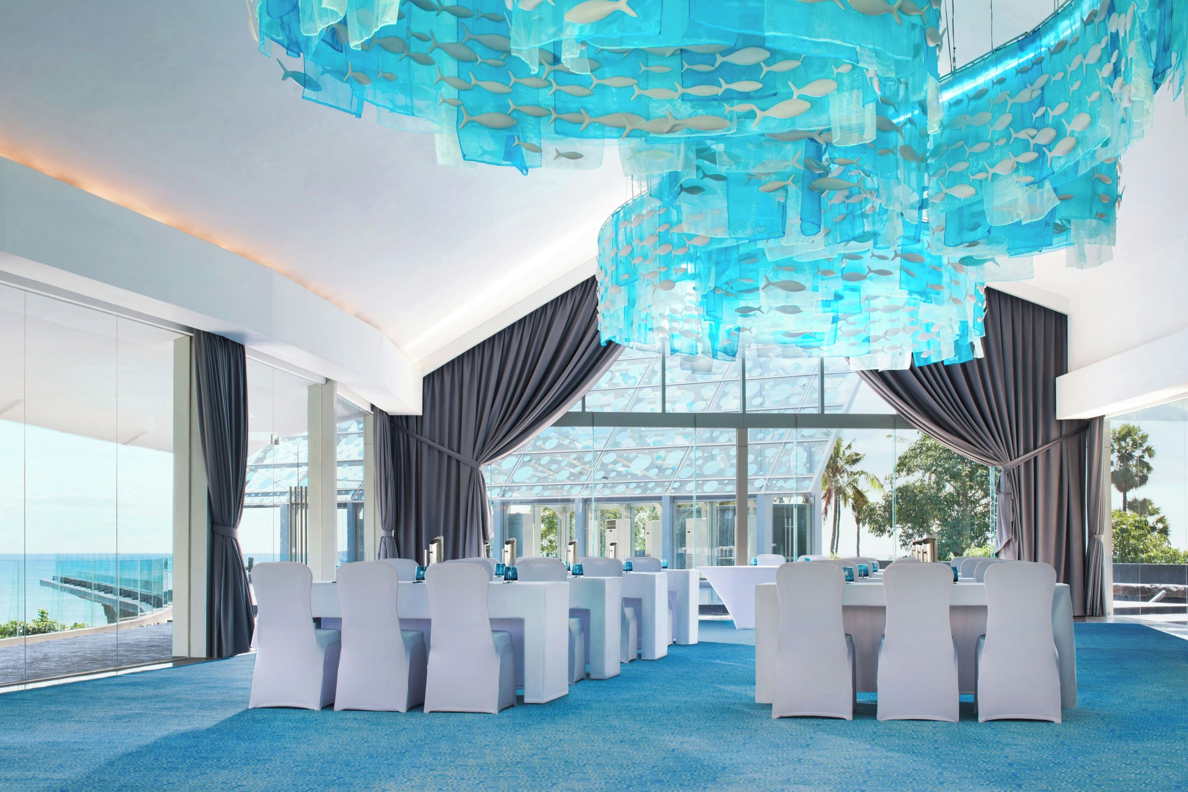A modern conference room with a glass ceiling, white chairs, and a blue carpet.