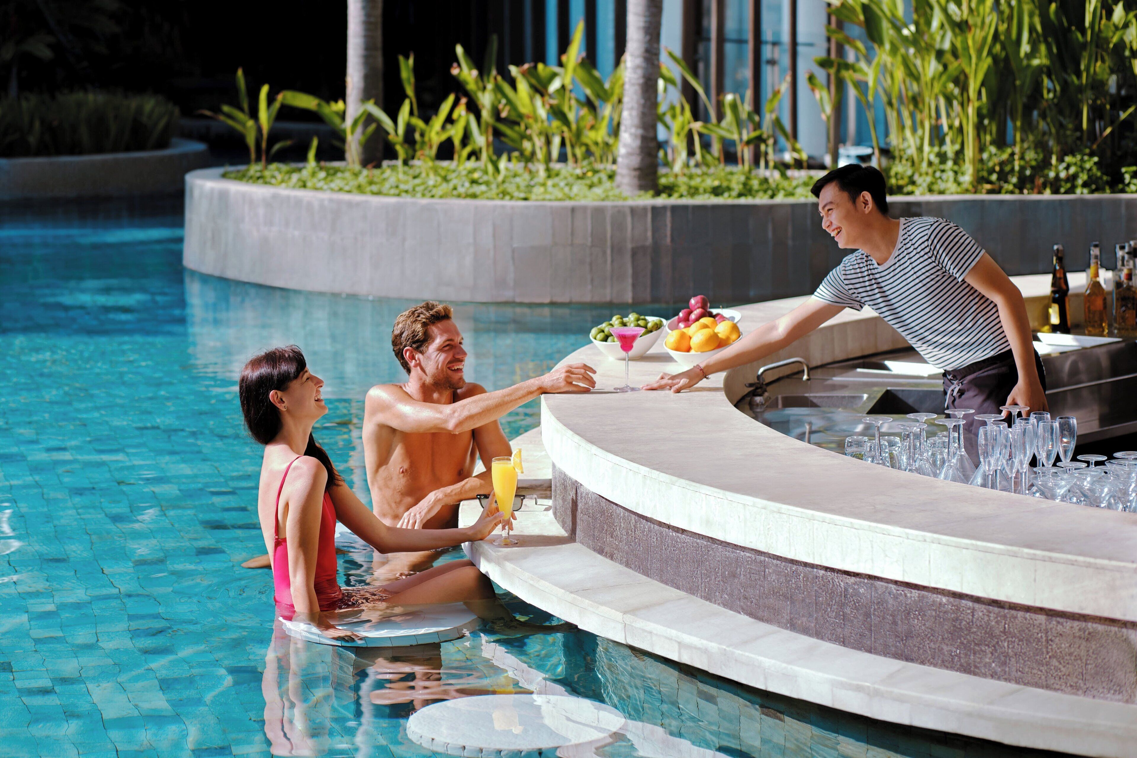 A poolside bar with a counter, a few people, and a bartender serving drinks.