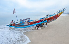 Un bateau traditionnel portant le nom « IMMA KARYA 1 » est amarré sur une plage de sable.