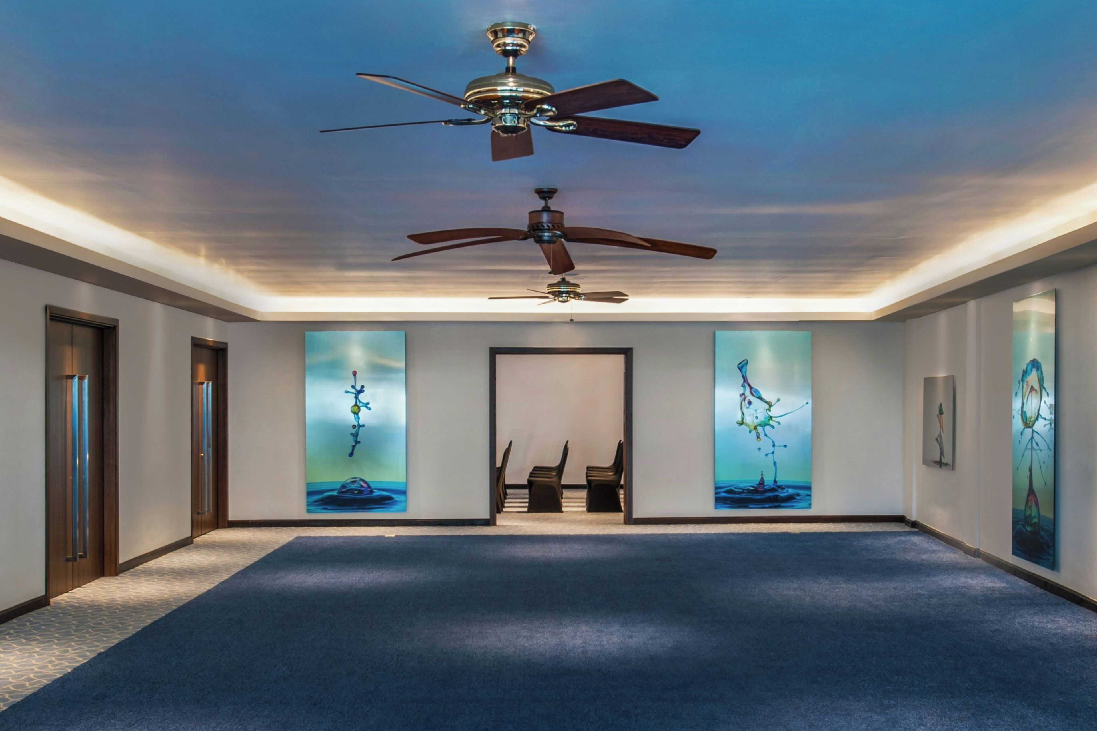 A hallway with two ceiling fans, a door on the left, and a staircase leading to an upper level.