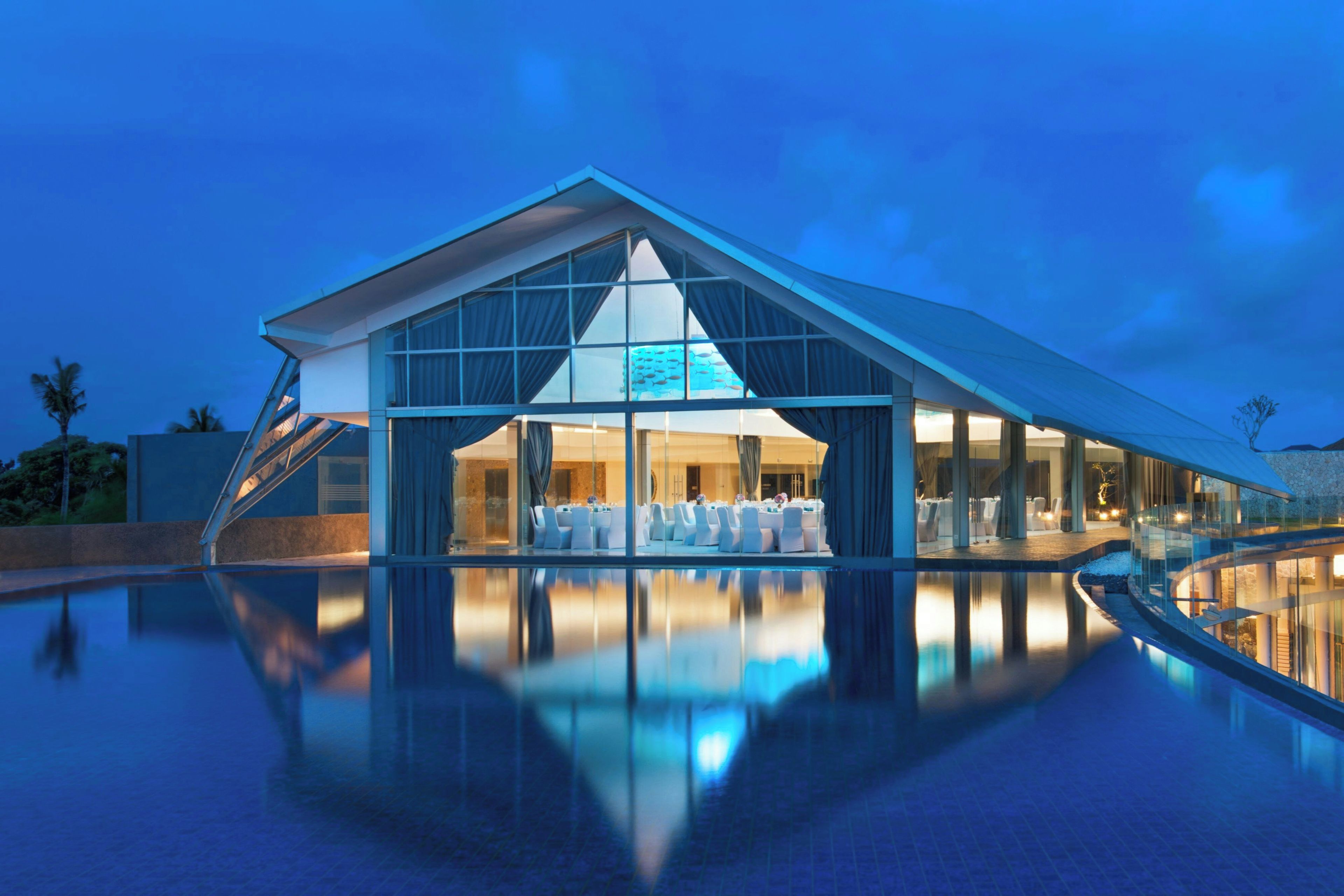 Un hotel moderno con fachada de vidrio, piscina y comedor con mesas y sillas.