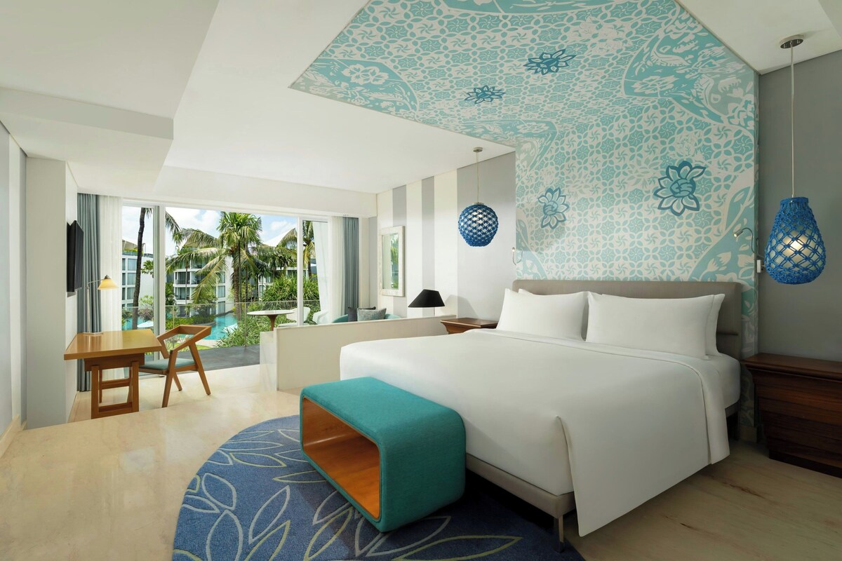 A modern hotel room with a large bed, a desk, and a view of a pool.