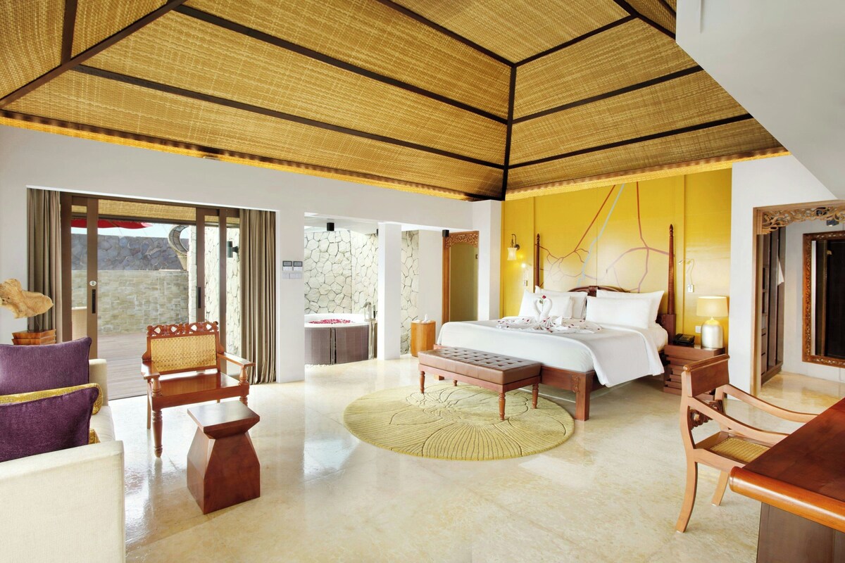 A spacious hotel room with a large bed, a sitting area with a round table, and a view of the outdoors.