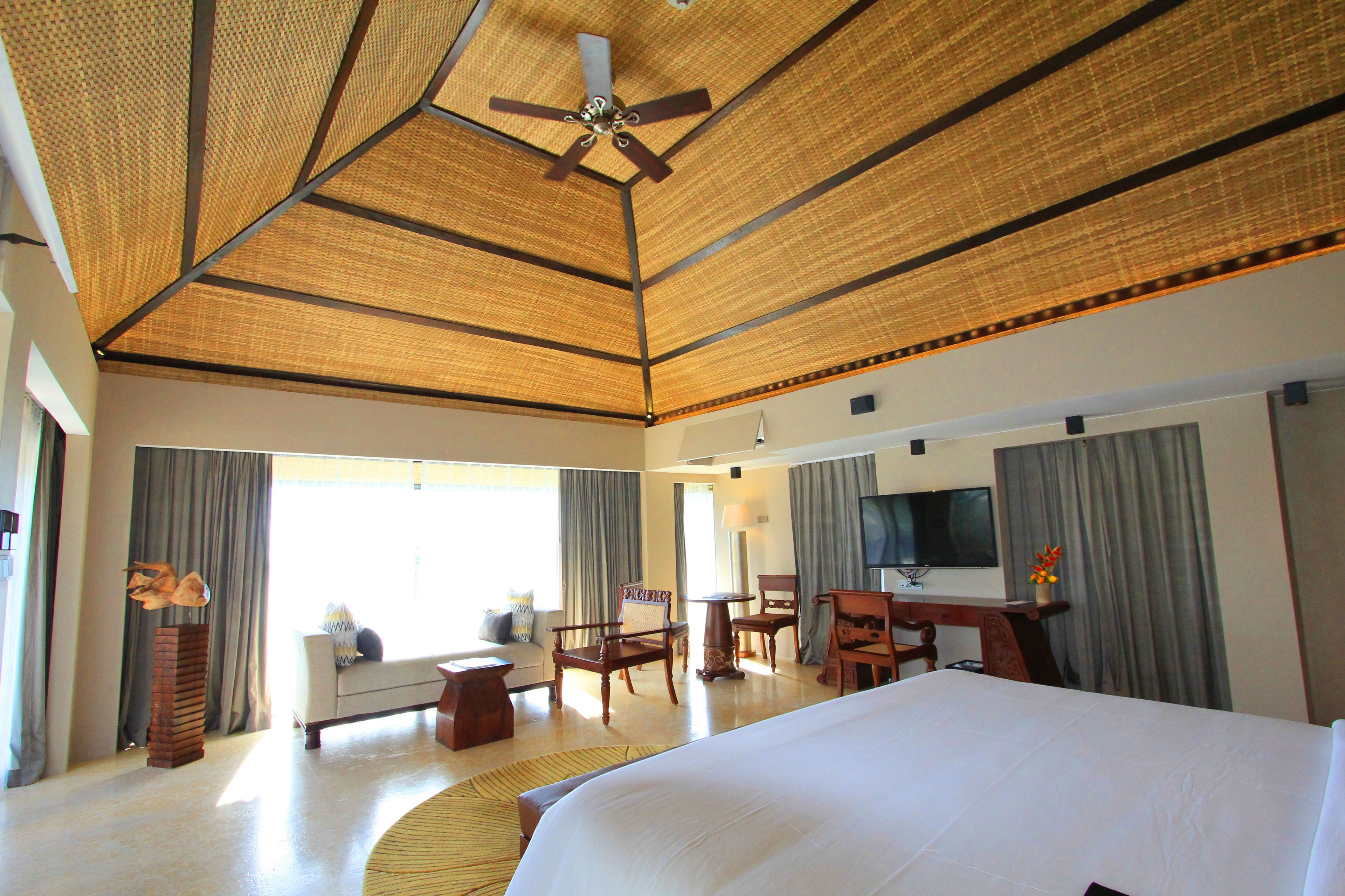 Une chambre d’hôtel spacieuse, dotée d’un grand lit, d’un ventilateur de plafond, d’une télévision à écran plat et d’un coin salon avec un canapé et des fauteuils.