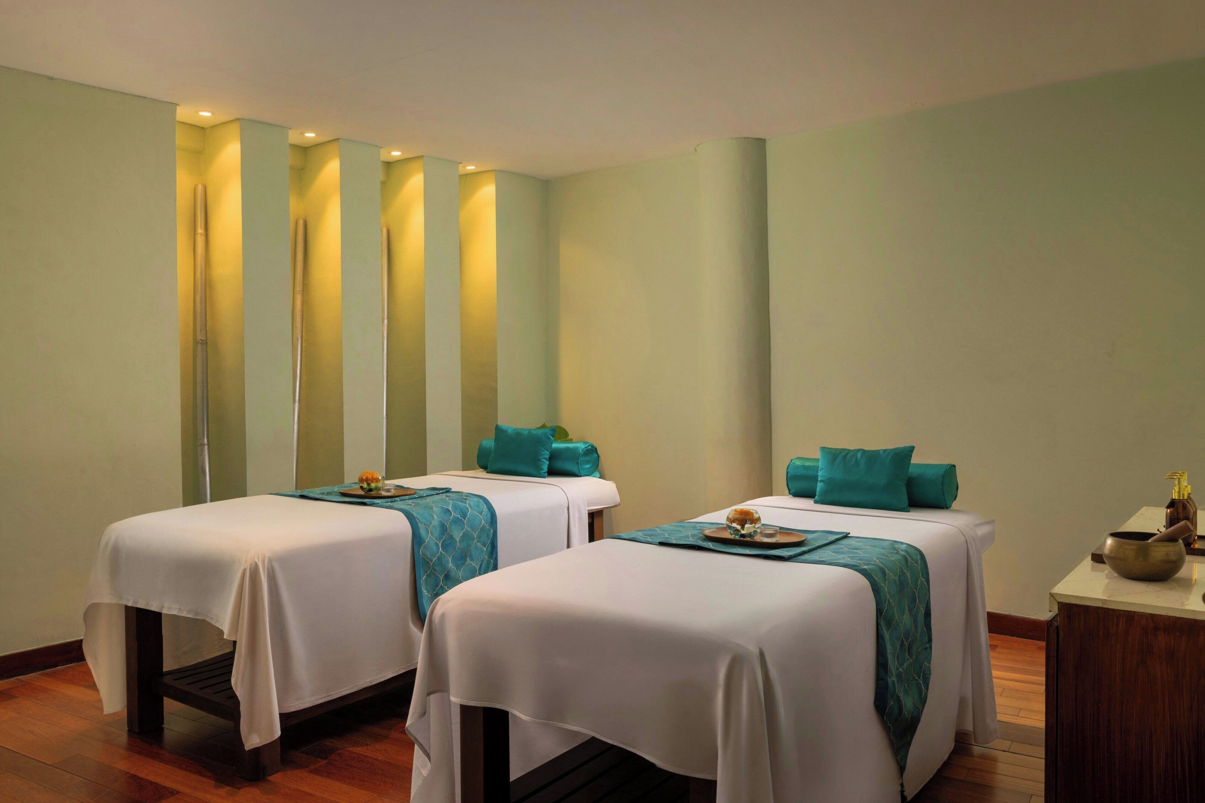 Deux lits simples avec des oreillers de couleur turquoise et une petite table sur laquelle se trouvent un bol et une bouteille.