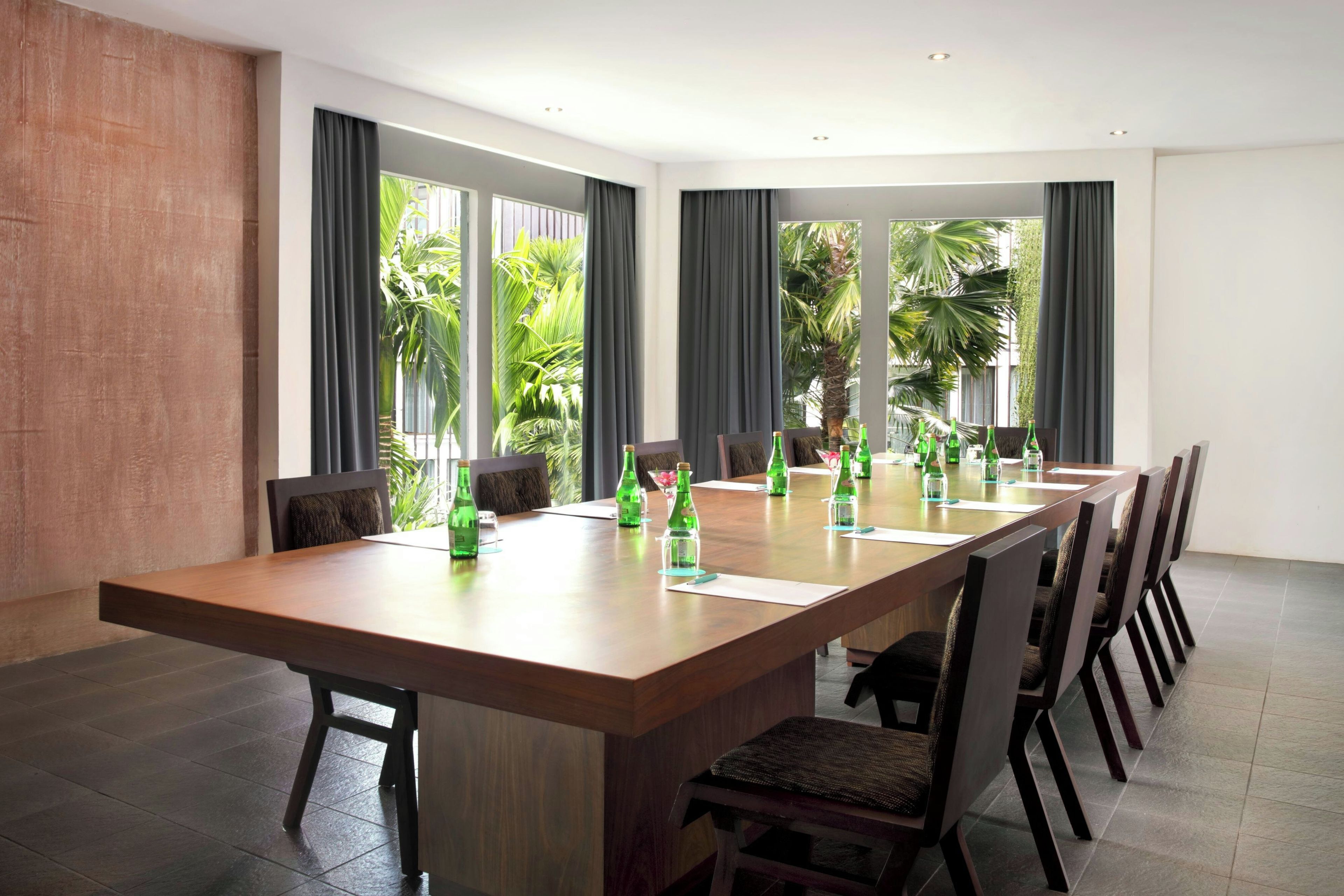 A conference room with a long table, chairs, and a view of palm trees through large windows.