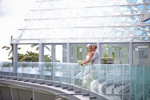 Un couple s’embrasse sur un balcon doté d’une rambarde en verre, avec vue sur une piscine.