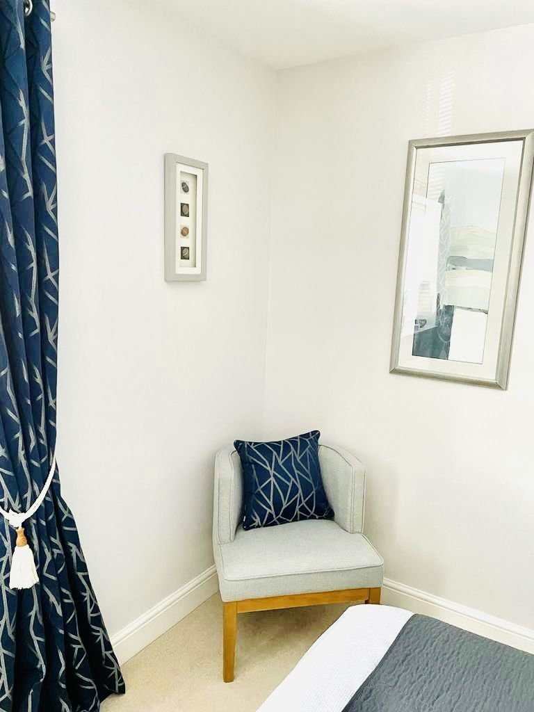 A small, neatly arranged bedroom with a bed, a chair, and a framed picture on the wall.