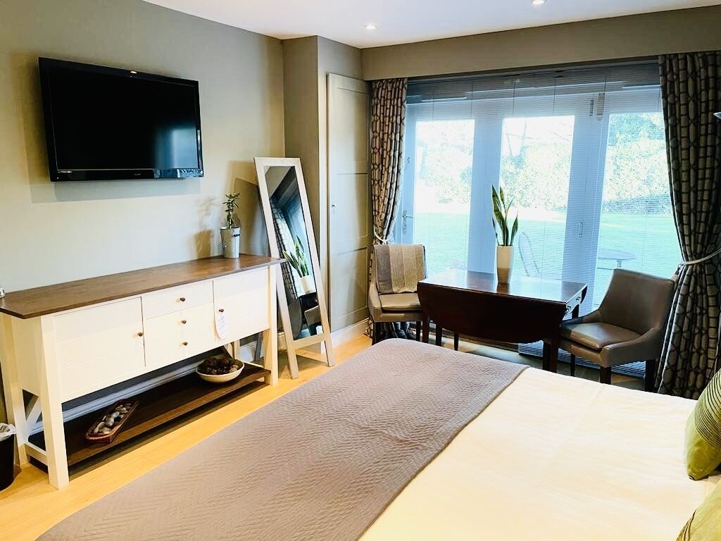 Habitación de hotel con cama, televisión, escritorio con silla y un ventanal con cortinas.