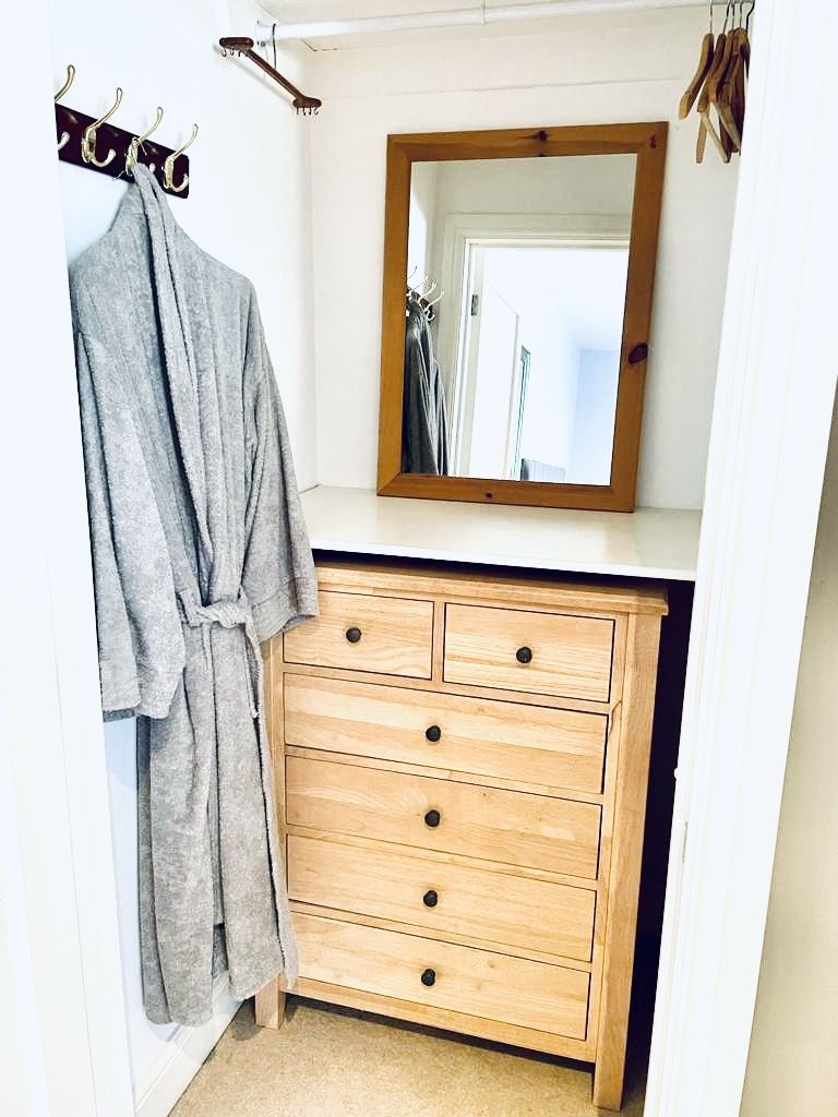 Un baño con tocador de madera, un espejo y una bata colgada en un perchero.