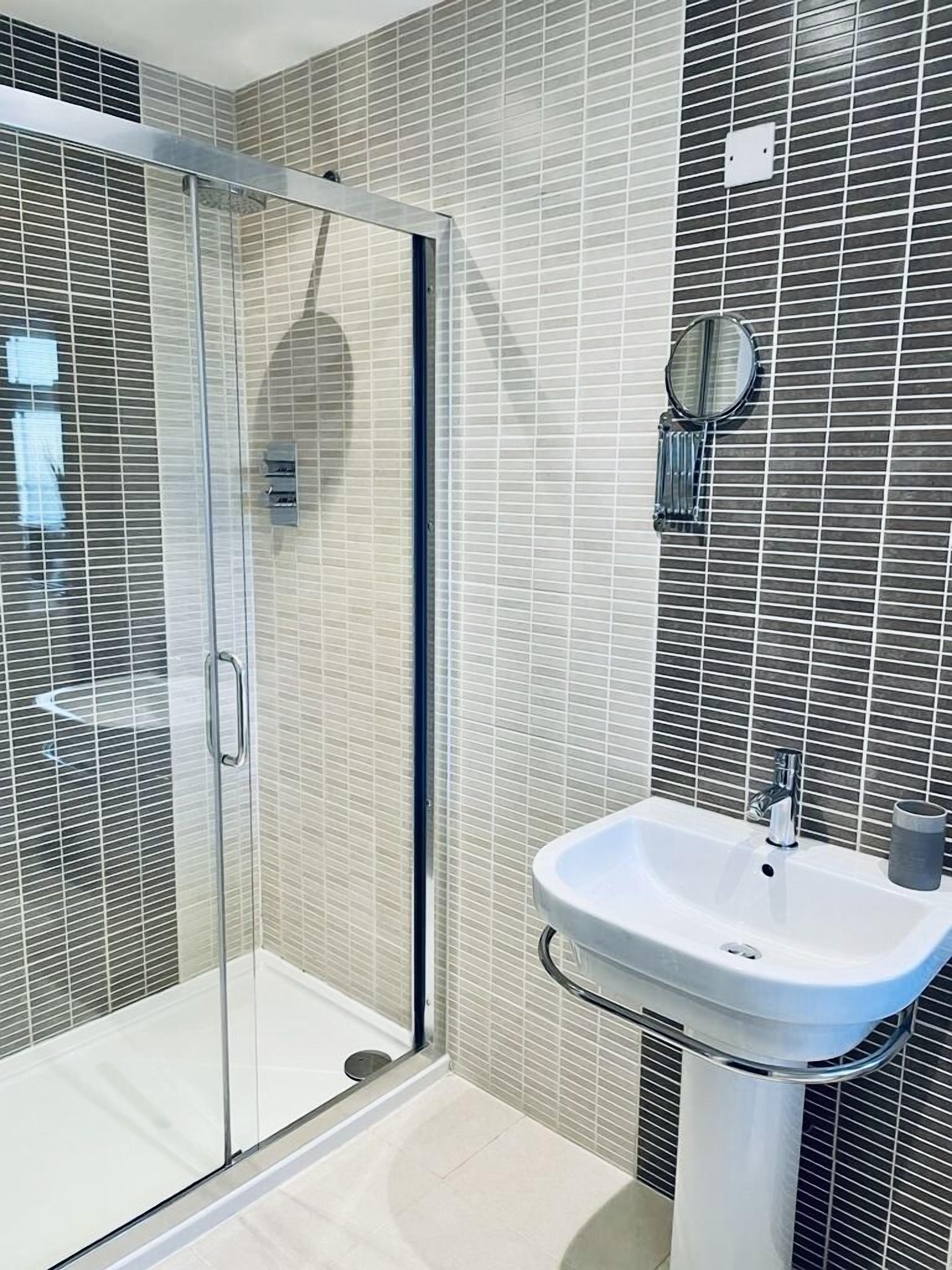 A modern bathroom with a glass shower enclosure, a white sink, and a mirror.