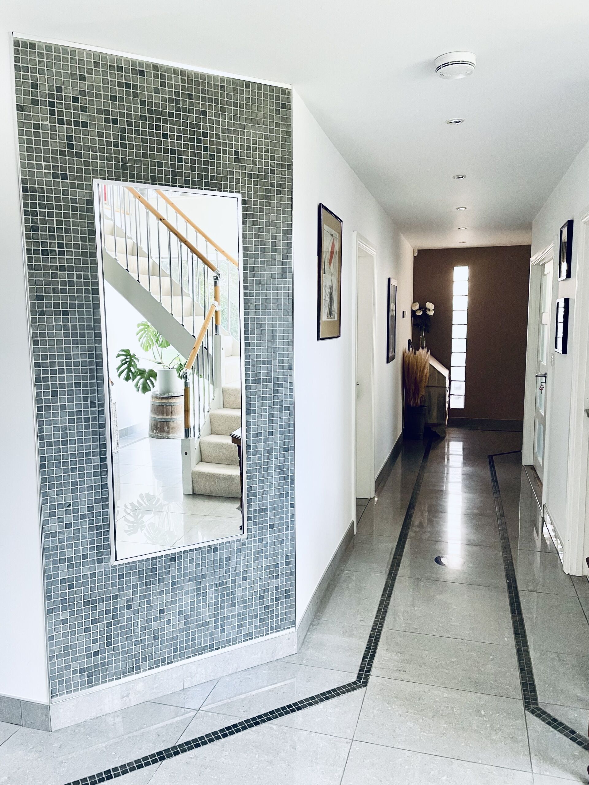 A hallway with a tiled wall, a staircase, and a door at the end.