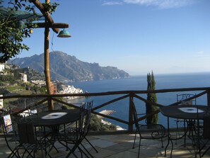 A terrace with outdoor seating overlooking a coastal view, including a mountain and the sea.