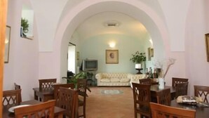 A dining area with wooden tables and chairs, a sofa, and a television in the background. - Villa Rina (Amalfi)