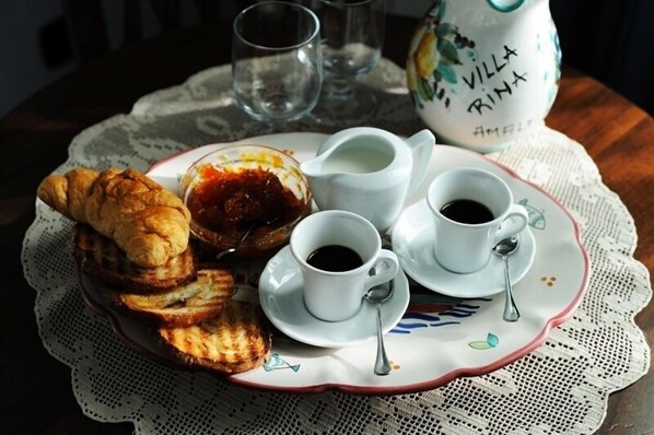 A breakfast tray with croissants, jam, and coffee cups on a lace tablecloth.