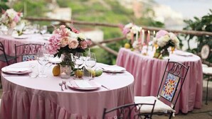 Round tables with pink tablecloths, floral centerpieces, and metal chairs with colorful backrests. - Villa Rina (Amalfi)