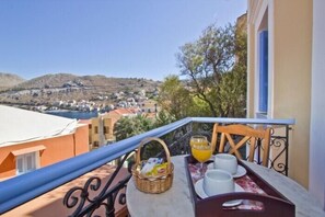 A balcony with a table set for breakfast, overlooking a hillside town. - Dorian Hotel (Symi)