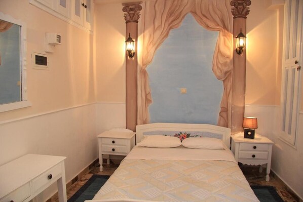 A bedroom with a bed, two nightstands, a window, and a wall-mounted air conditioning unit. - Dorian Hotel (Symi)