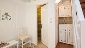 Una habitación blanca con una silla de madera, una mesita y un armario decorado con motivos florales.