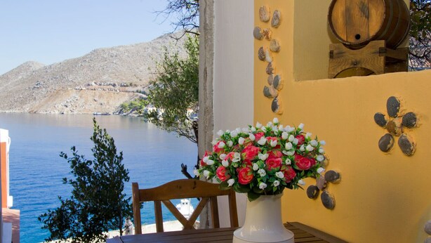 Una mesa de madera con un jarrón blanco de flores, una silla de madera y una vista de un lago con montañas al fondo.
