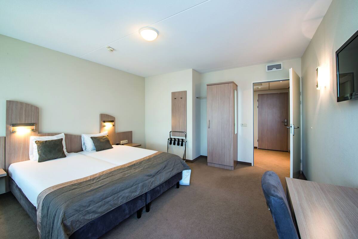 A hotel room with a large bed, bedside tables, a desk, and a TV mounted on the wall.