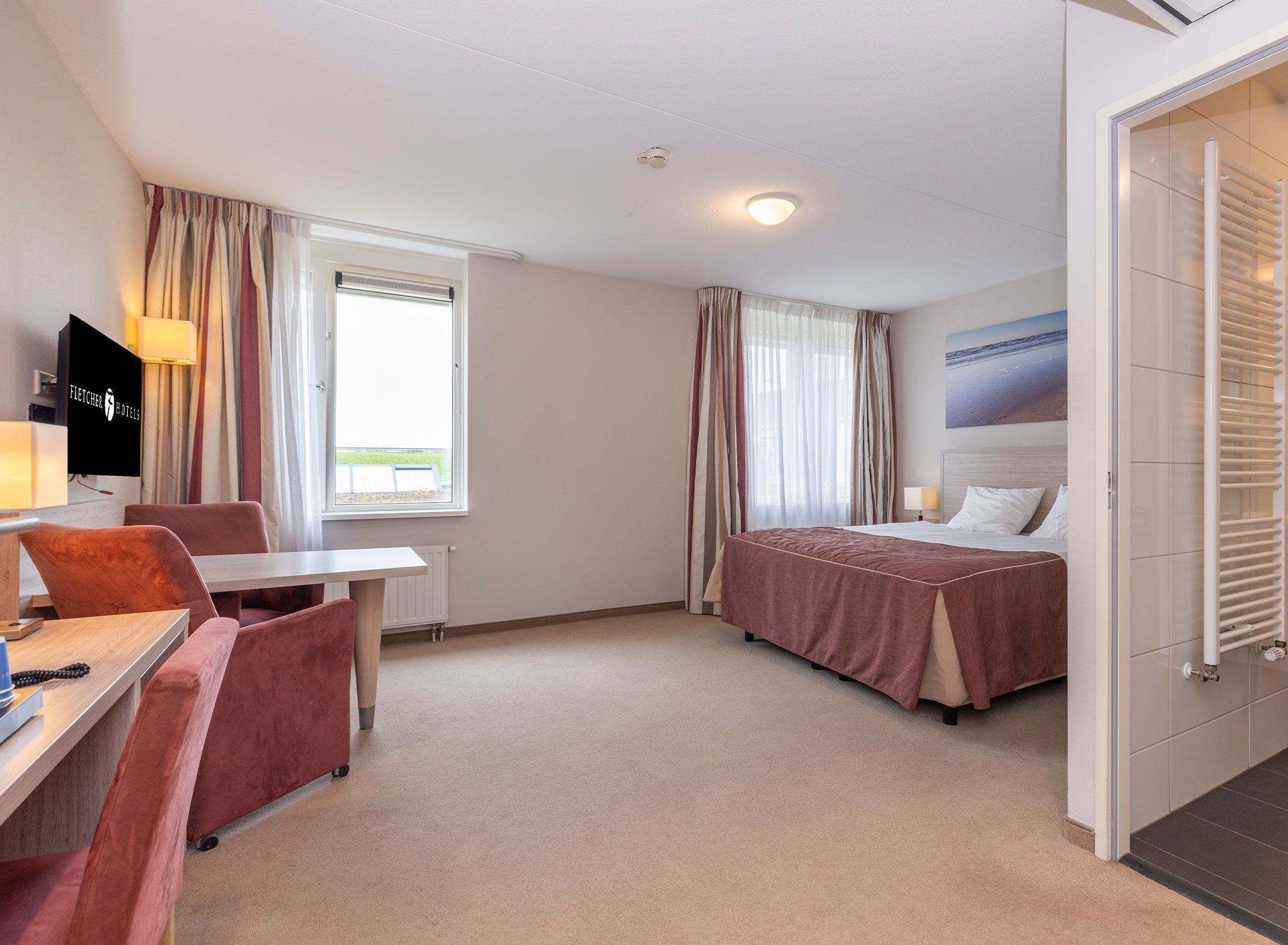 A hotel room with a bed, a desk, a chair, a TV, and a window.