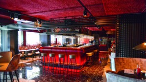 Una zona de bar con taburetes, una barra y un área de estar con mesas y sillas.