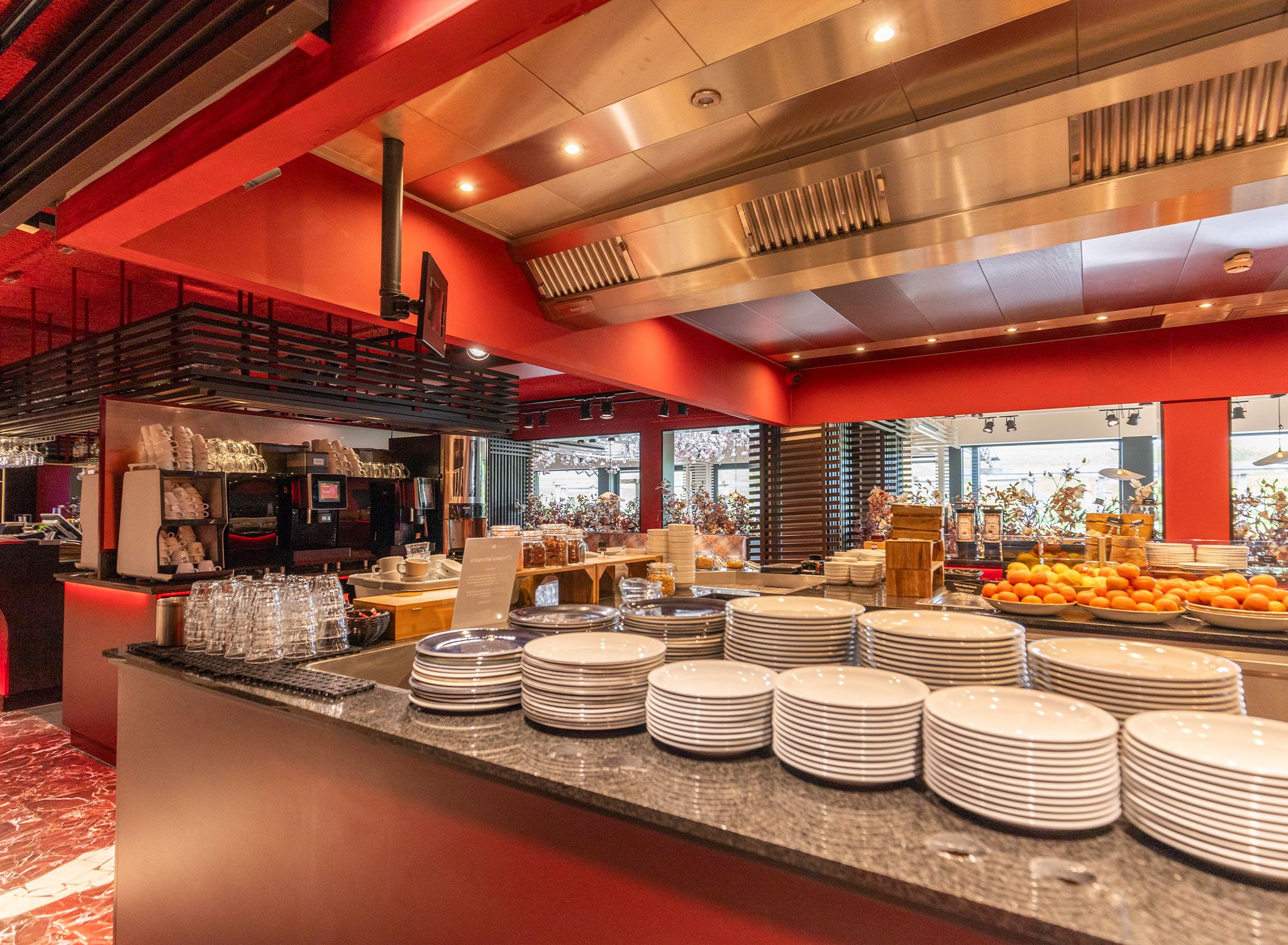 A buffet area with stacks of plates and bowls, a coffee station, and a fruit display.