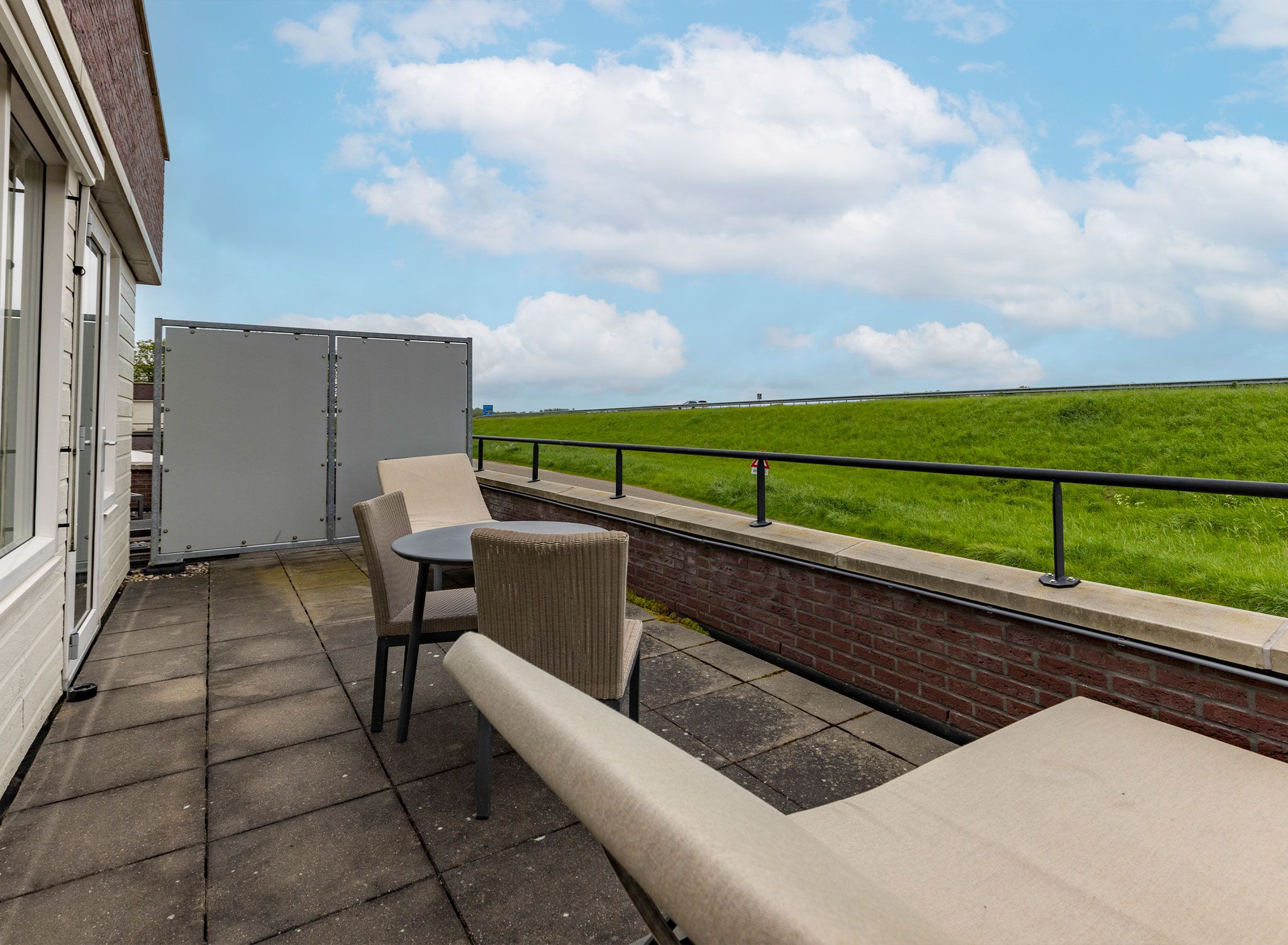 A balcony with a table and chairs, a view of a green field, and a clear sky.