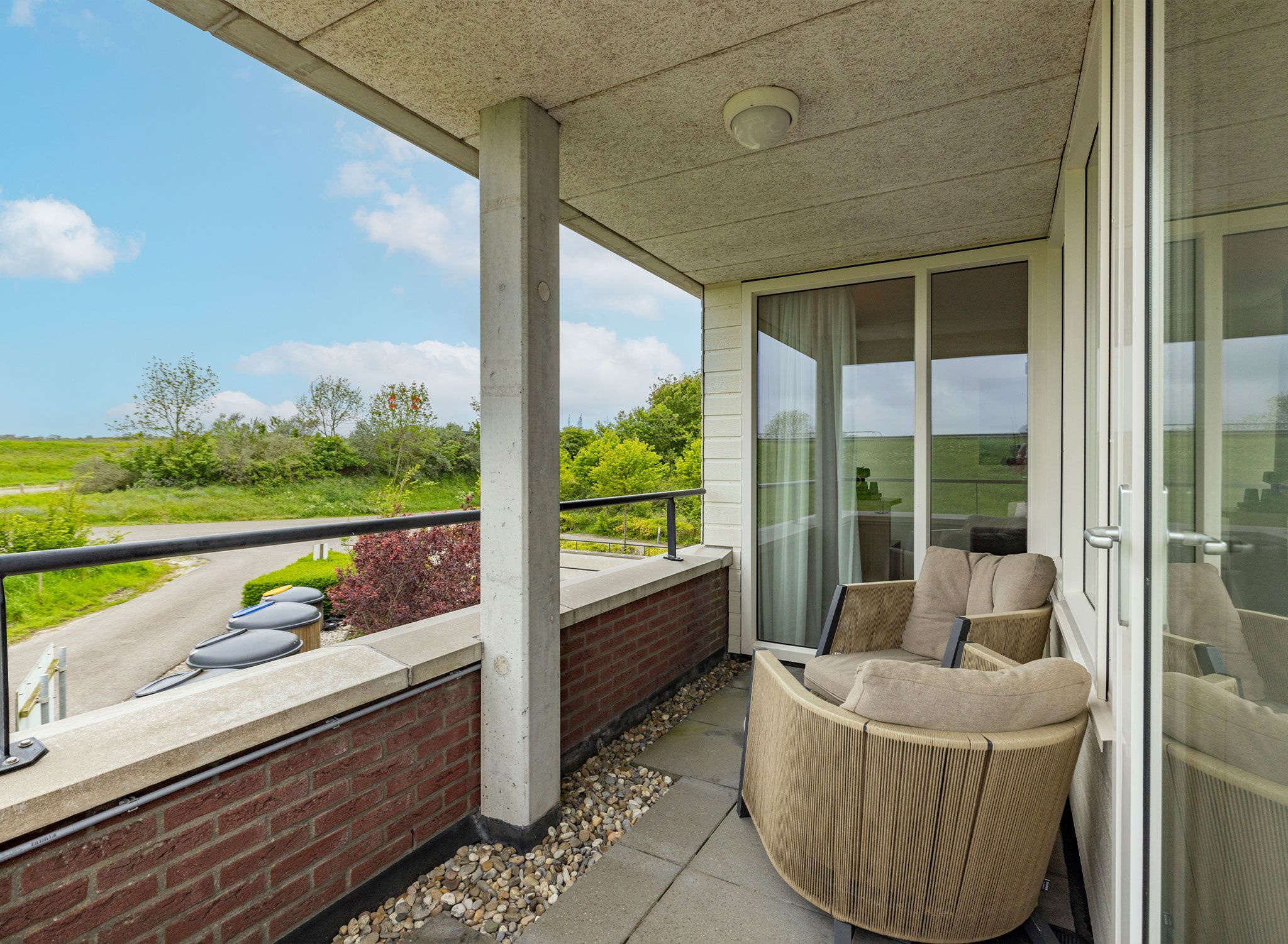 A balcony with a wicker chair and a view of a road and greenery.