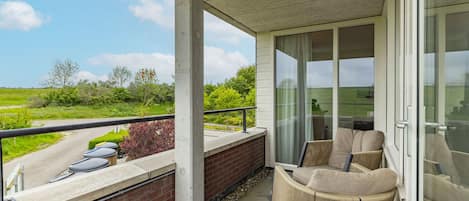 A balcony with a wicker chair and a view of a road and greenery.