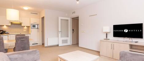 Una habitación de hotel moderna con televisión de pantalla plana, sofás grises, una mesa de centro de madera, una zona de cocina con microondas y una mesa de comedor.