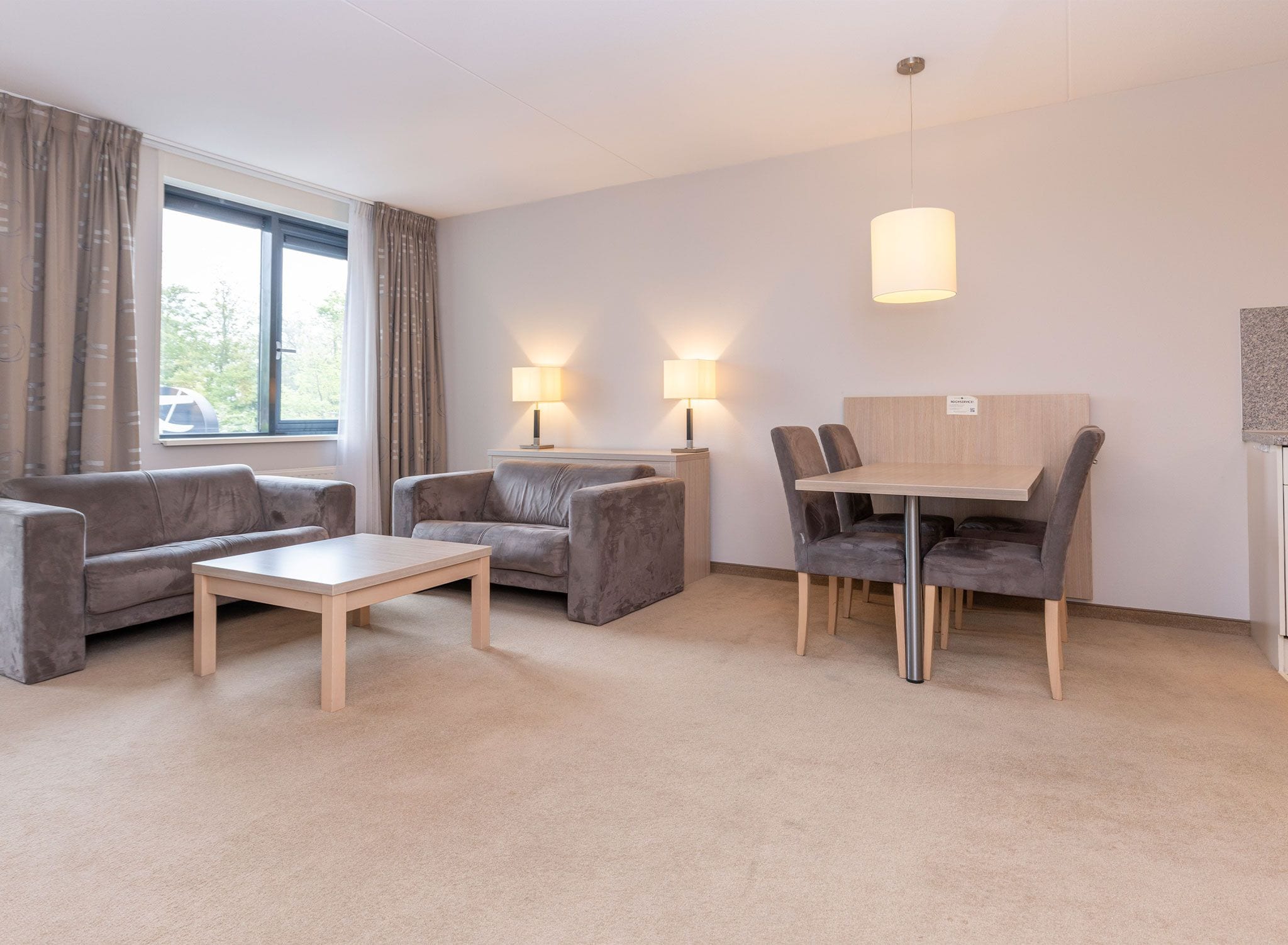 A hotel room with a sofa, two armchairs, a small table, a dining table with chairs, and two lamps.