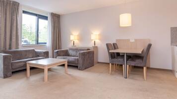 Ein Hotelzimmer mit einer Couch, zwei Sesseln, einem kleinen Tisch, einem Esstisch mit Stühlen und zwei Lampen.