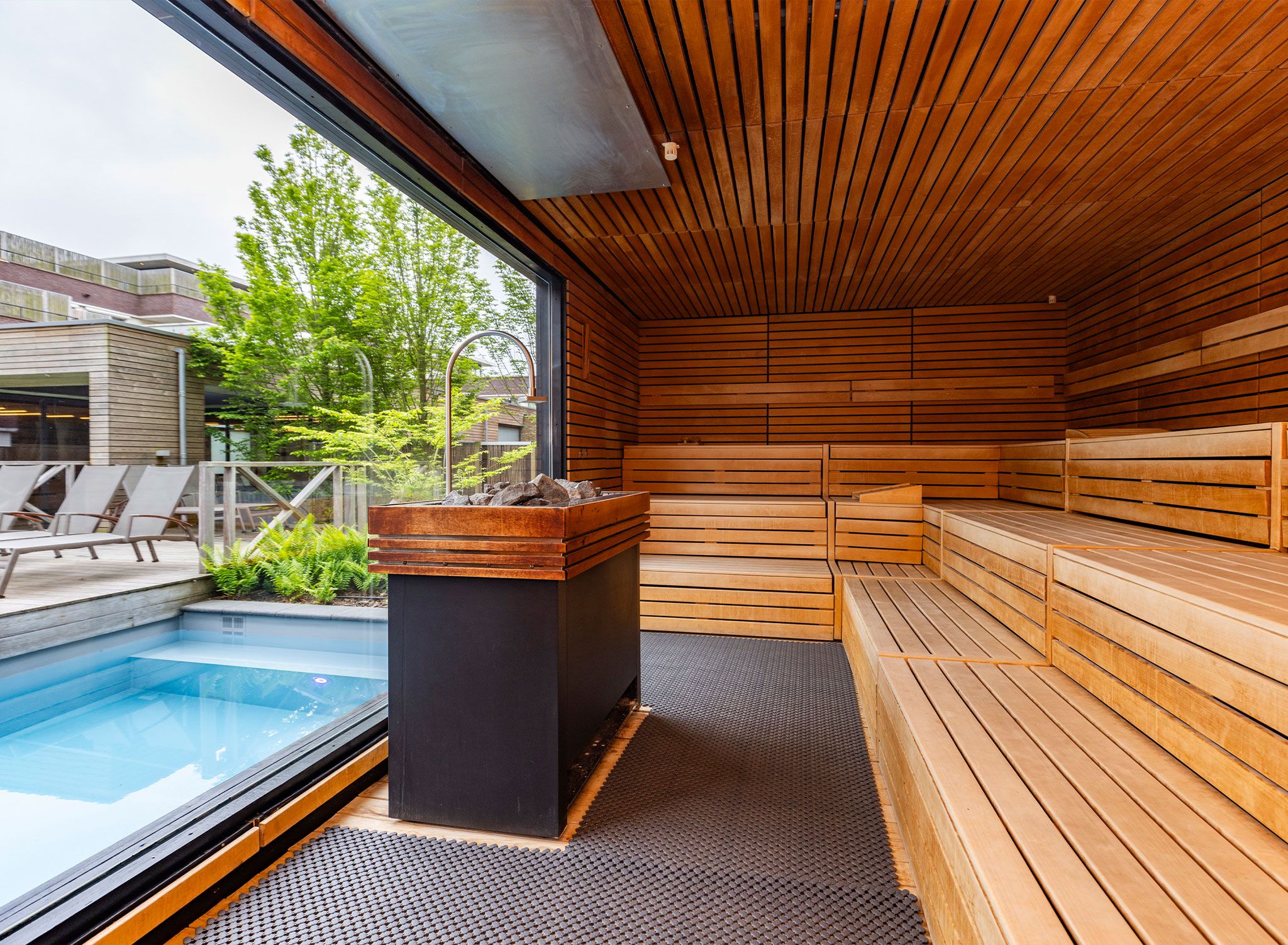 A sauna with wooden benches and a stone bench, a pool, and a view of the outside.