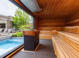 Uma sauna com bancos de madeira e um banco de pedra, uma piscina e vista para o exterior.