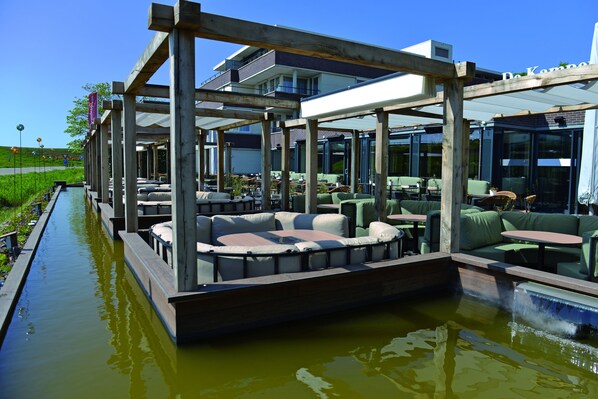 An outdoor seating area with tables and chairs, a water feature, and a view of a building in the background.