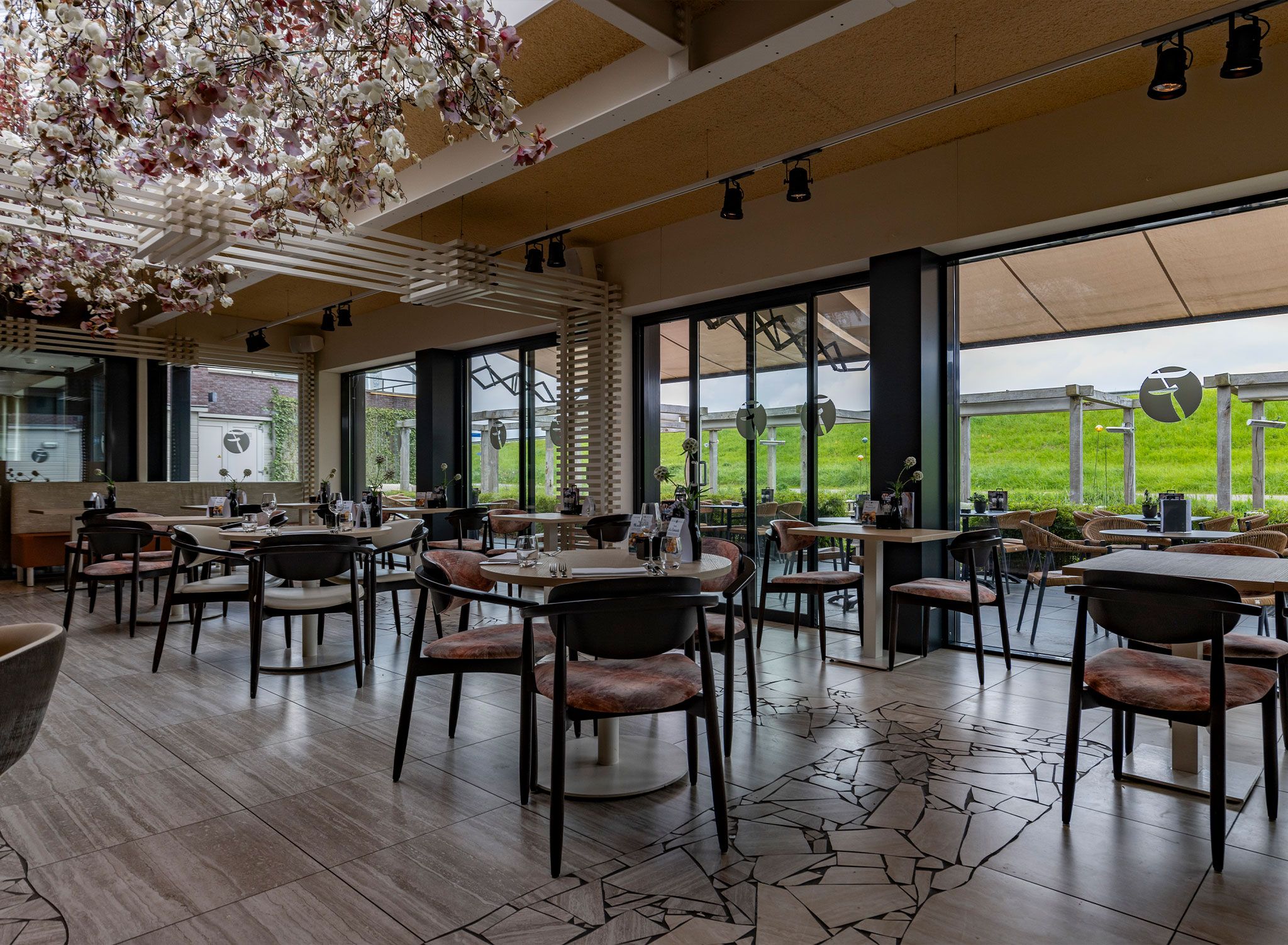 Un restaurante con mesas dentro, ventanas amplias y vistas al exterior.