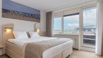 A hotel room with a large bed, two bedside lamps, a window with a view, and a painting on the wall.