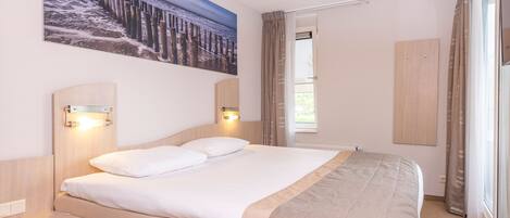 A hotel room with a large bed, bedside tables, a painting on the wall, and a window with curtains.