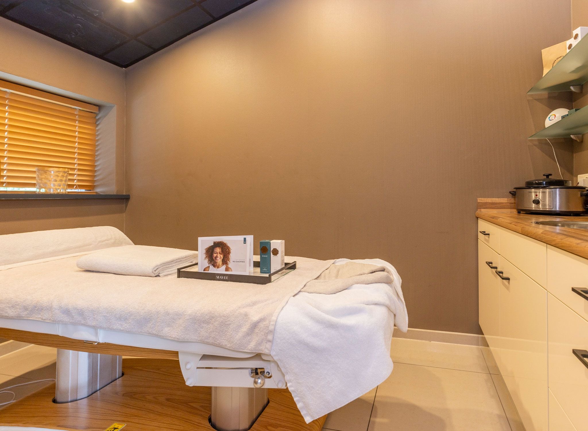 Een schone, moderne kamer met een bed, een klein nachtkastje en een raam met luxaflex.