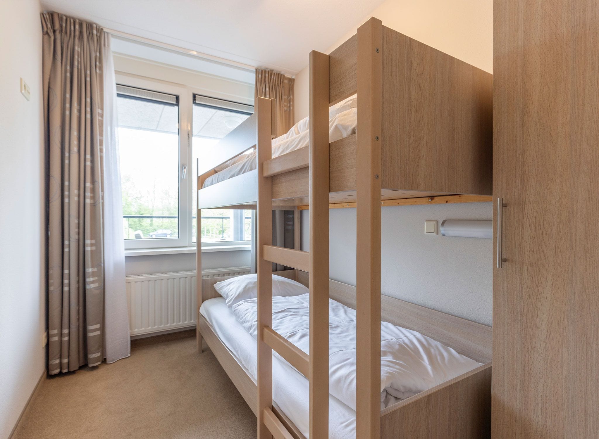 A bunk bed room with a window, curtains, and a radiator.