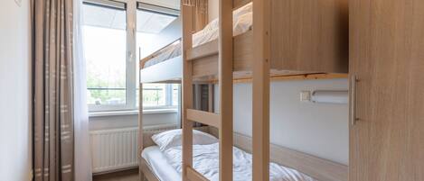 A bunk bed room with a window, curtains, and a radiator.