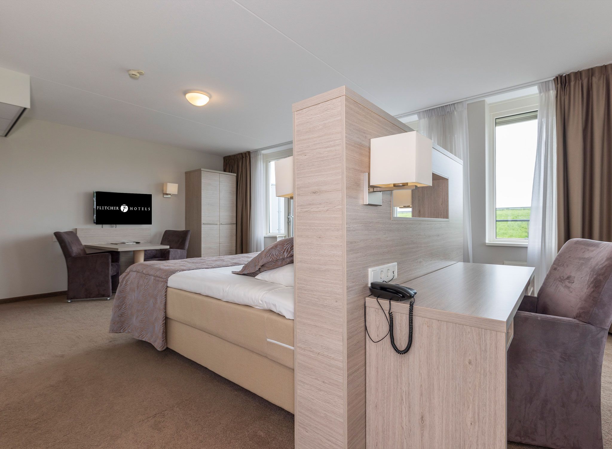 A hotel room with a bed, a desk, a chair, a TV, and a phone.