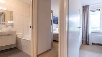 A hotel room with a bathroom, a bed, and a window with curtains.