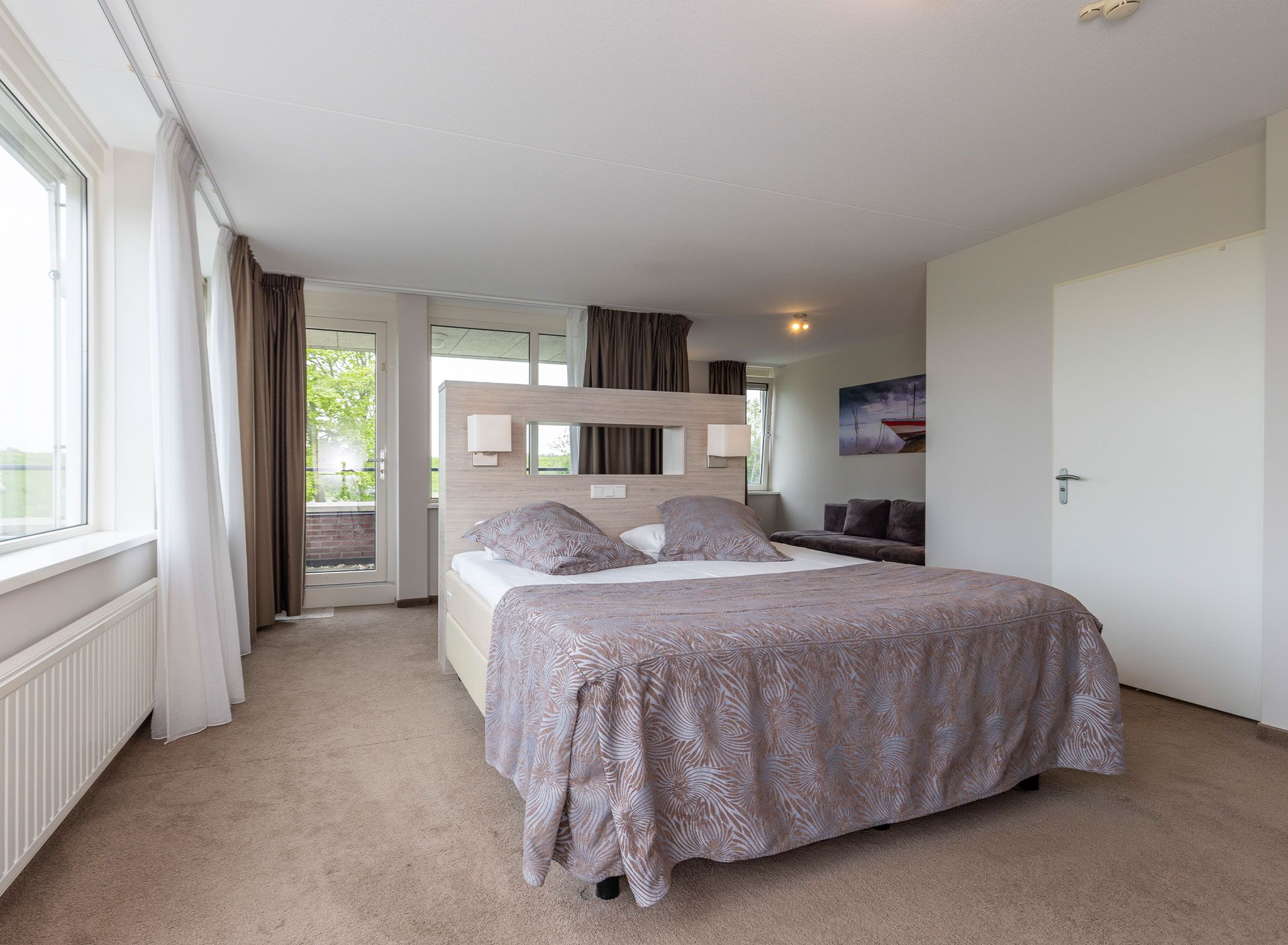 A bedroom with a bed, a window, a door, and a painting on the wall.