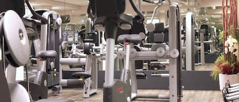 A gym with various exercise machines, a mirrored wall, and a wooden floor.