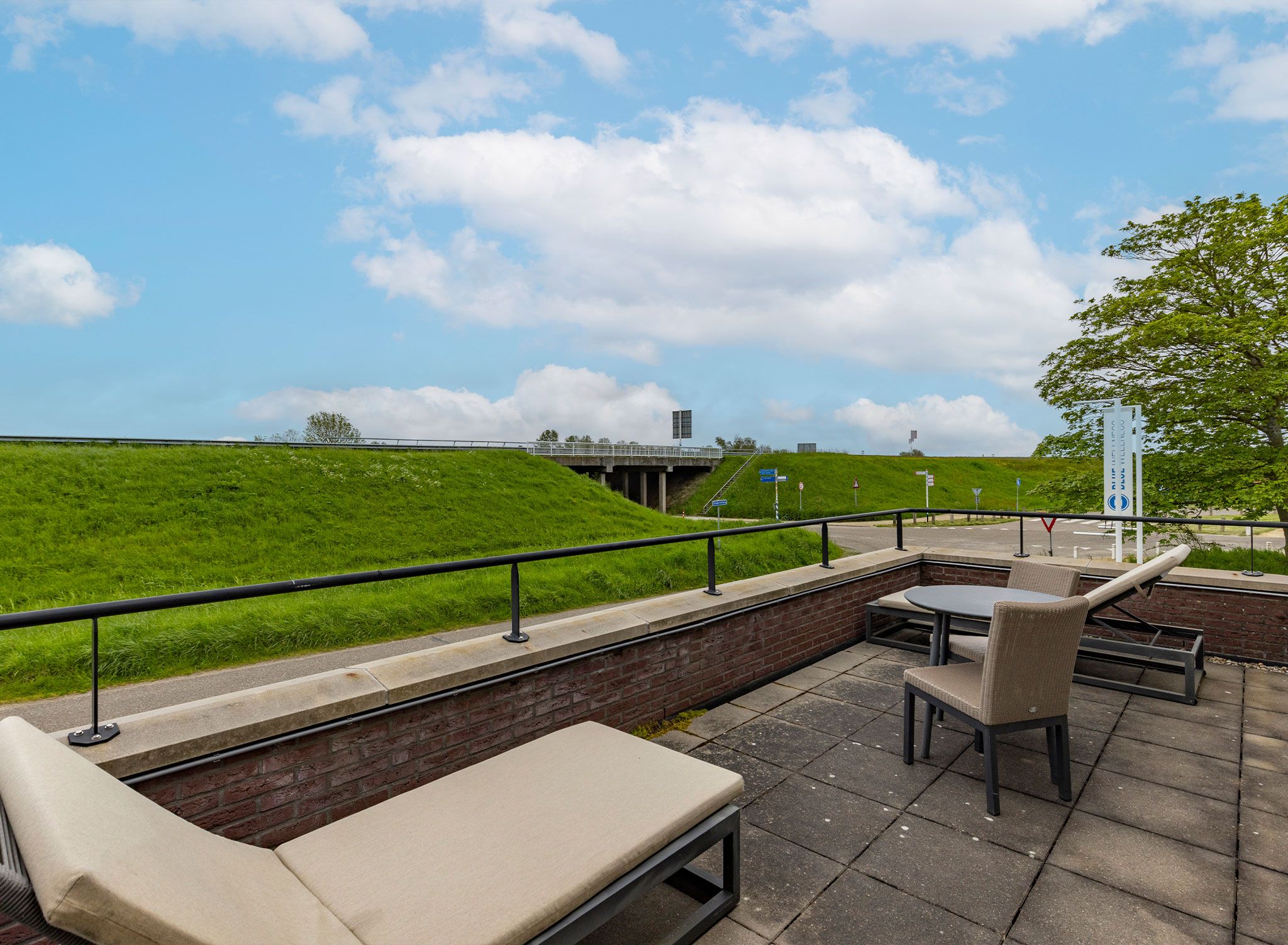 An outdoor seating area with a view of a green hill and a bridge in the distance.